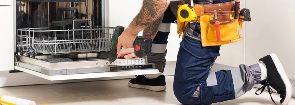 Closeup repair and installation of dishwasher, male worker with tool in uniform