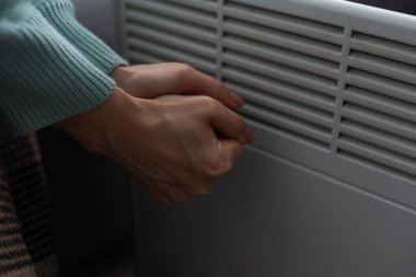 Evde elektrikli ısıtıcının yanında ellerini ısıtan kadın, yakın çekim..