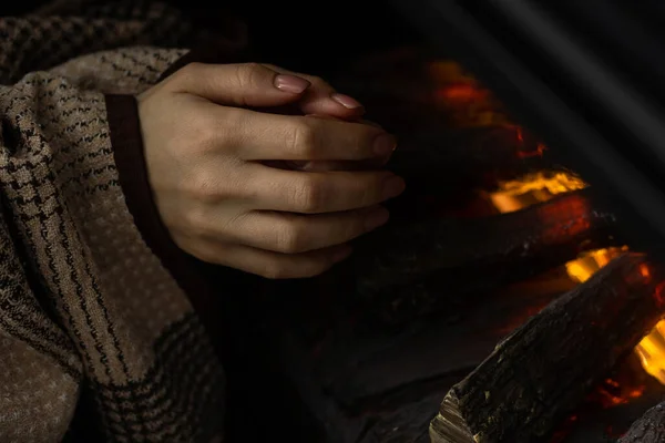 Young woman warming hands near fireplace at home. Concept of heating season