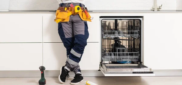 Closeup repair and installation of dishwasher, male worker with tool in uniform
