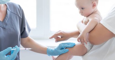 Doktor beyaz arka planda bebek aşısı yapıyor.