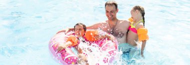Denizde tropik bir tatil köyünde mavi yüzme havuzunda oynayan mutlu bir aile. Yaz tatilleri konsepti