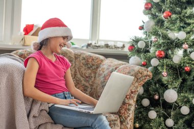 Mutlu küçük bir kız evdeki Noel ağacının altında bir hediye açar ve bilgisayar aracılığıyla büyükannesi ve büyükbabasıyla iletişim kurar. Yılbaşı ve evde yeni yıl tatili konsepti.