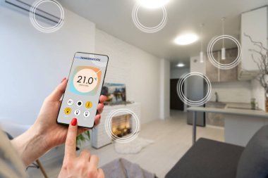Ekranda akıllı ev yazılımı uygulaması olan cep telefonuna odaklan, dijital cihazlı kablosuz hafif müzik sıcaklık düzenlemesi, klima iklim kontrolü, iot, sanal asistan.