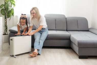 Anne ve çocuk elektrikli ısıtıcının yanında ellerini ısıtıyorlar.
