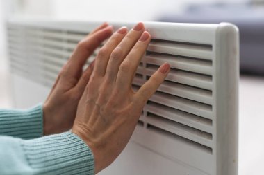 Kazaklı bir kadının yakın çekimi beyaz duvarın arkasındaki akünün üzerinde ellerini ısıtıyor. Makro kadın eli fotoğrafı, kopyalama alanı. Kışın gaz tasarrufu kavramı. Avrupa 'da gaz krizi.