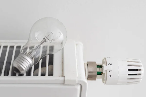heating, energy crisis and consumption concept - light bulb on radiator at home