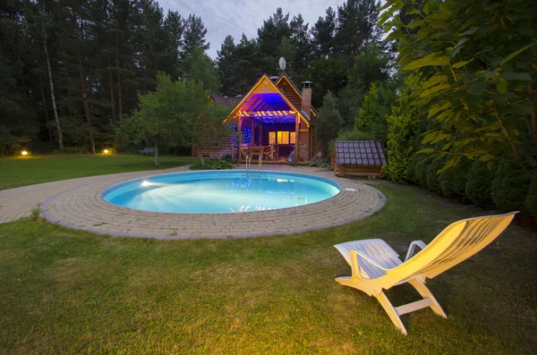 Uma piscina com cadeira perto de casa de madeira à noite Fotos De Bancos De Imagens
