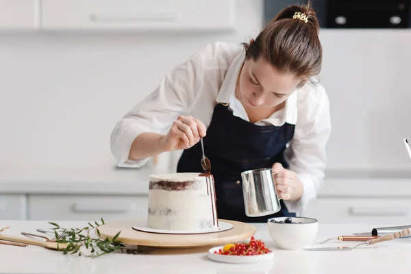 Feliz bom olhar chef pasteleiro feminino de pé com seu bolo ao fazer. Colocar creme em um bolo de aniversário. Imagem De Stock