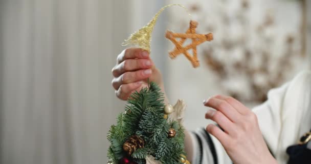 Primer plano de las manos de una mujer, que decora el árbol de Navidad y cuelga una estrella de oro. Nochebuena, humor, vacaciones — Vídeo de stock