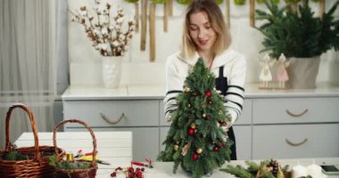 Çiçekçi iş başında. Kadın çiçekçi köknar şeklinde güzel Noel süslemesi yapıyor, küçük Noel ağacı.
