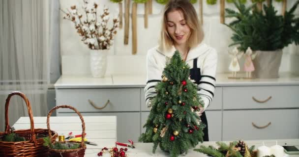 Ανθοπωλείο στη δουλειά. Γυναίκα ανθοπώλης κάνει όμορφη διακόσμηση των Χριστουγέννων σε σχήμα ελάτης, μικρό χριστουγεννιάτικο δέντρο — Αρχείο Βίντεο