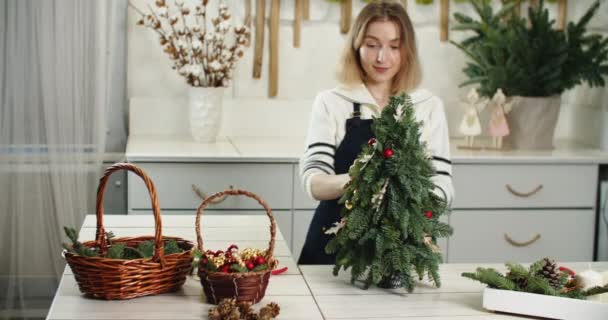 Ανθοπωλείο στη δουλειά. Γυναίκα ανθοπώλης κάνει όμορφη διακόσμηση των Χριστουγέννων σε σχήμα ελάτης, μικρό χριστουγεννιάτικο δέντρο — Αρχείο Βίντεο