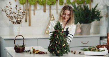 Çiçekçi iş başında. Kadın çiçekçi köknar şeklinde güzel Noel süslemesi yapıyor, küçük Noel ağacı.