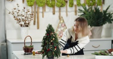 Çiçekçi iş başında. Kadın çiçekçi köknar şeklinde güzel Noel süslemesi yapıyor, küçük Noel ağacı.