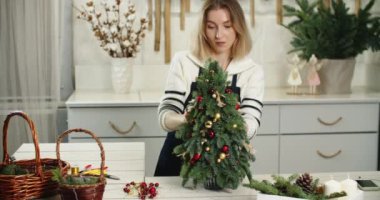 Çiçekçi iş başında. Kadın çiçekçi köknar şeklinde güzel Noel süslemesi yapıyor, küçük Noel ağacı.