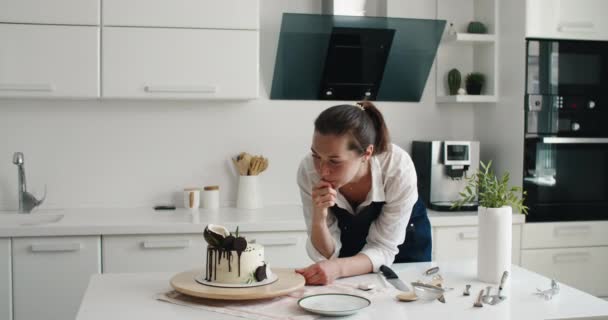 Pastry chef in the kitchen makes cake. Cooking at home. Delicious and beautiful homemade cakes, pastry recipes. A young woman in an apron in the kitchen cut the cake — Vídeo de Stock
