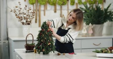 Çiçekçi iş başında. Kadın çiçekçi köknar şeklinde güzel Noel süslemesi yapıyor, küçük Noel ağacı.