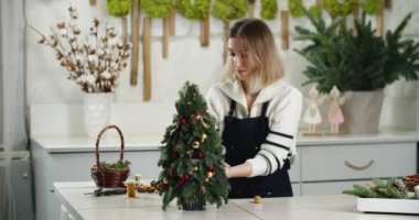 Çiçekçi iş başında. Kadın çiçekçi köknar şeklinde güzel Noel süslemesi yapıyor, küçük Noel ağacı.