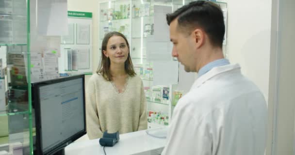 Pagamento in farmacia. Farmacista sorridente che propone alla donna un terminale di pagamento mentre usa il suo carrello di credito. Acquisto senza contatto — Video Stock