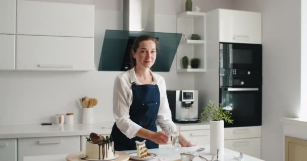 Κουρασμένη γυναίκα ζαχαροπλάστης πίνει νερό στην κουζίνα, ενώ κάνει μια τούρτα — Αρχείο Βίντεο