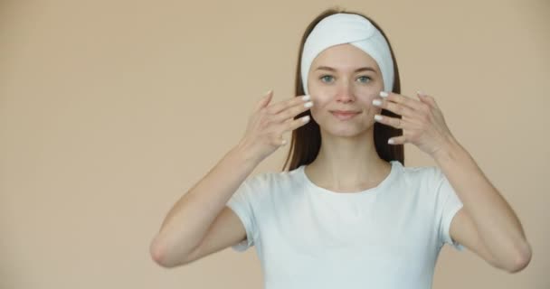 Una giovane donna felice si gira e applica la crema sul viso. Trattamenti benessere, cura del corpo e del viso — Video Stock