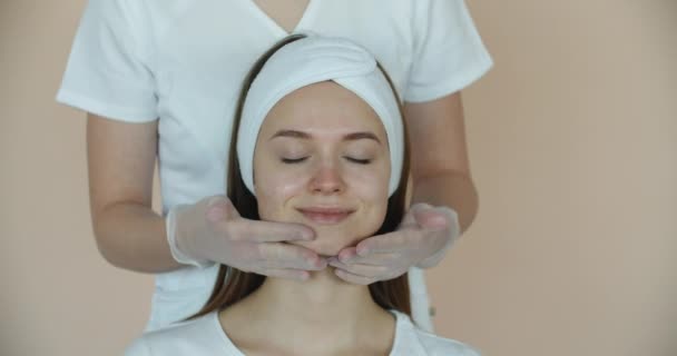 Gyönyörű nő kötéssel a fején kapok arcmasszázs, kozmetikai terápia fürdés után, spa kezelések a nők — Stock videók