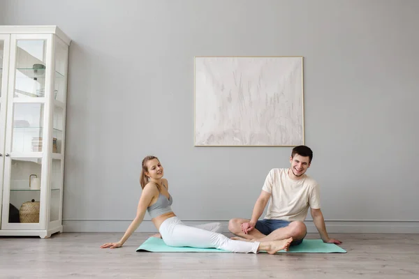 Pareja joven practicando acro yoga sobre estera en la casa juntos. Descanso después del ejercicio. —  Fotos de Stock