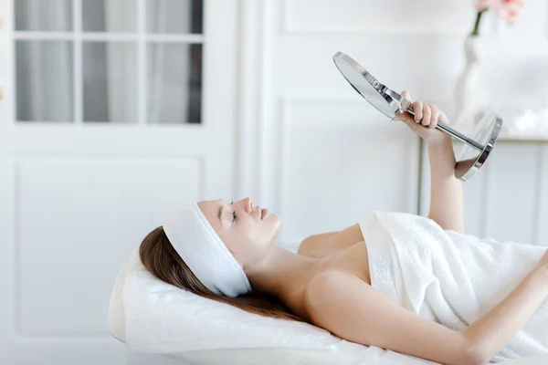 Spa prosedürleri aynaya baktıktan sonra tatmin olmuş müşteri kadın. güzellik endüstrisi konsepti.