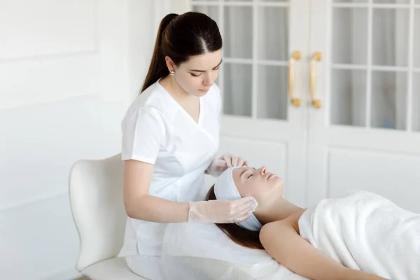 Kadın bir kozmetik uzmanı estetik tıp kliniğindeki bir müşteri için yüz işlemleri yapıyor. Kozmetik uzmanı ya da dermatolog kaplıcada ya da kuaförde kadınlara masaj yapıyor..