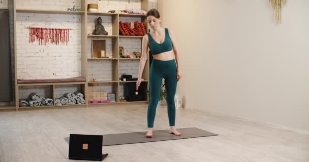 Übungen im Yoga-Studio. Sportliches Mädchen beim Yoga-Planken, während es Online-Tutorial auf Laptop anschaut, freier Platz — Stockvideo