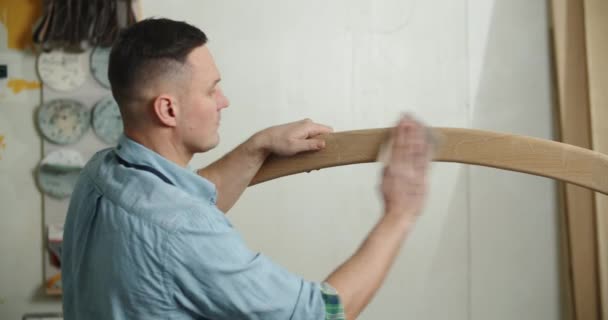 Плотник работает в мастерской. Плотник шлифует деревянную деталь наждачной бумагой. — стоковое видео