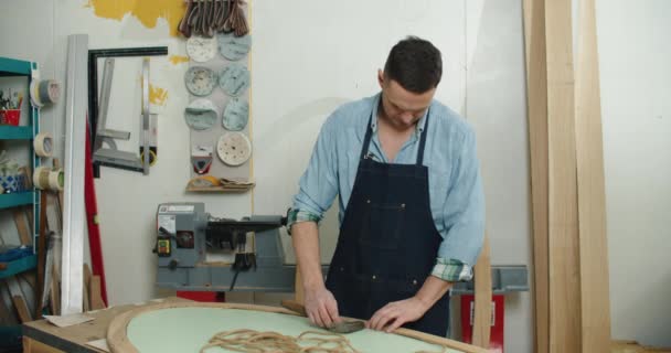 Tesař, který pracuje s kladivem a hřebíky. Připíchne lano na dřevěnou část. — Stock video
