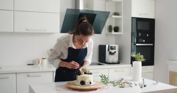 Mujer joven pastelera decora delicioso pastel con hojas decorativas — Vídeo de stock