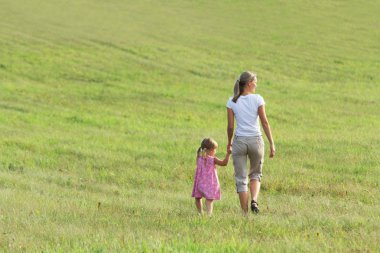 Mother with daughter go on grass in clean floor