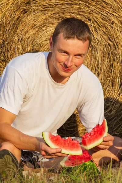 Der junge Mann isst eine leckere Wassermelone — Stockfoto