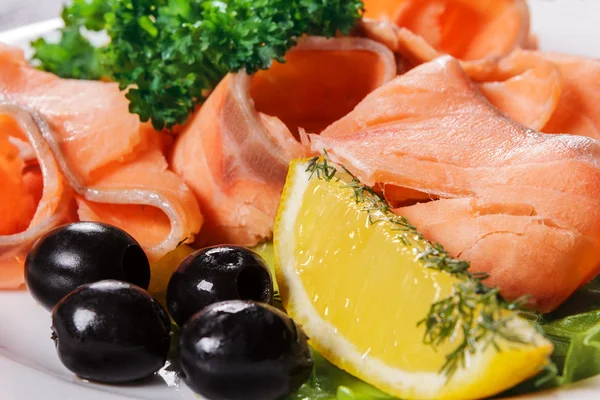 Scheiben roter Fisch mit Zitrone und Oliven auf Teller — Stockfoto