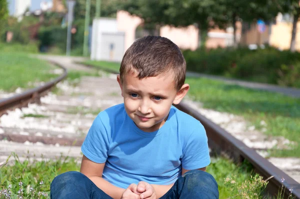 Lonely little boy sitting on a rails — Stock Photo, Image