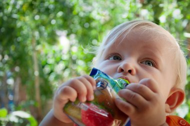 little blonde girl eats fruit puree in the park in summer, healthy baby food