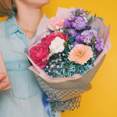 Hands holding bouquet of beautiful flowerson yellow background. Toned picture