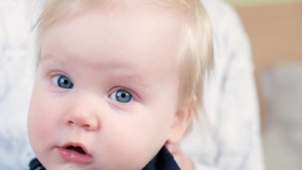 Un bébé de 9 mois s'assoit sur les genoux de sa mère et regarde la caméra avec ses yeux bleus. — Video