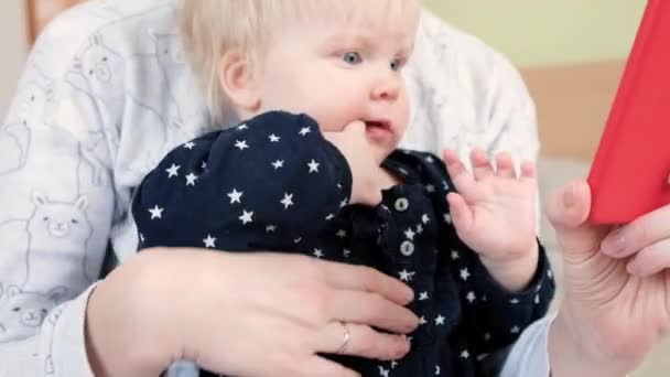 Een 9 maanden oude baby in haar moeders armen kijkt naar de telefoon — Stockvideo