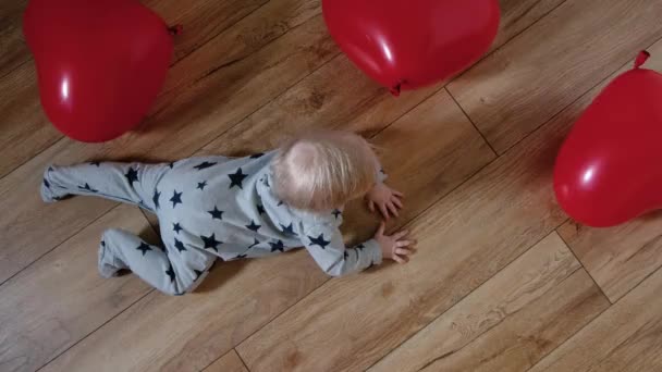 Een 9 maanden oude baby kruipt op de vloer omringd door rode ballen. Bovenaanzicht — Stockvideo