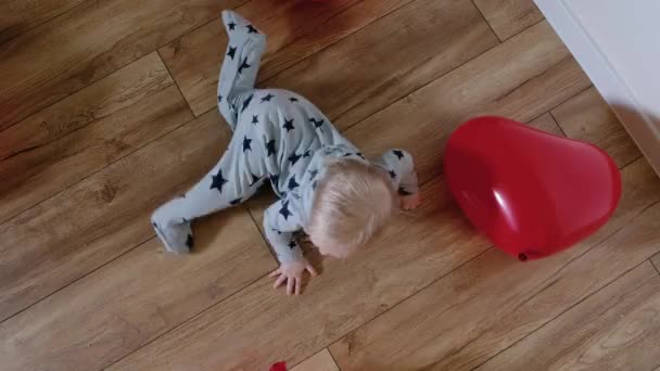 Een 9 maanden oude baby kruipt op de vloer omringd door rode ballen. Bovenaanzicht — Stockvideo