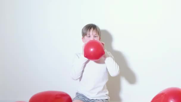 Een 7-jarige jongen speelt met een rode ballon in de vorm van een hart. Valentijnsdag Concept — Stockvideo