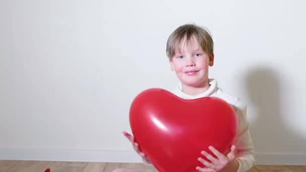Ένα 7χρονο αγόρι παίζει με ένα κόκκινο μπαλόνι σε σχήμα καρδιάς. Έννοια Ημέρα του Αγίου Βαλεντίνου — Αρχείο Βίντεο