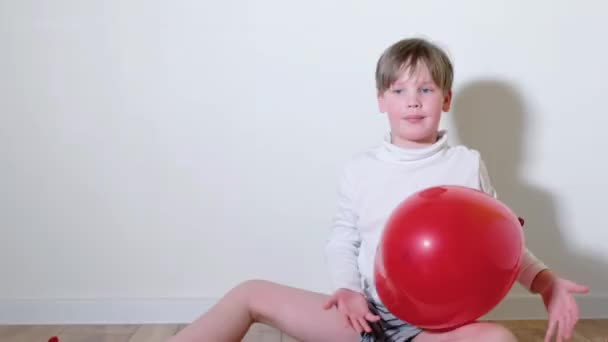 Um menino de 7 anos está brincando com um balão vermelho na forma de um coração. Conceito Dia dos Namorados — Vídeo de Stock