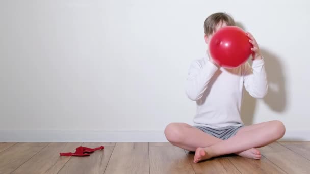 Een 7-jarige jongen speelt met een rode ballon in de vorm van een hart. Valentijnsdag Concept — Stockvideo