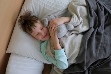 Üzgün hasta bir çocuk yatakta yatıyor. Grip, solunum enfeksiyonu ya da virüs ihtimaline karşı baş ağrısı ve yüksek ateş. Hastalık salgını.