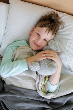 Çocuk pelüş bir oyuncakla yatakta ateşle yatıyor.